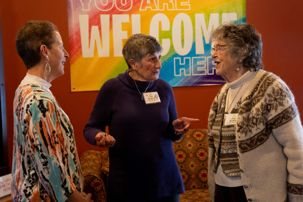 A few members of our pastoral care team stand chatting together in front of our "you are welcome" sign