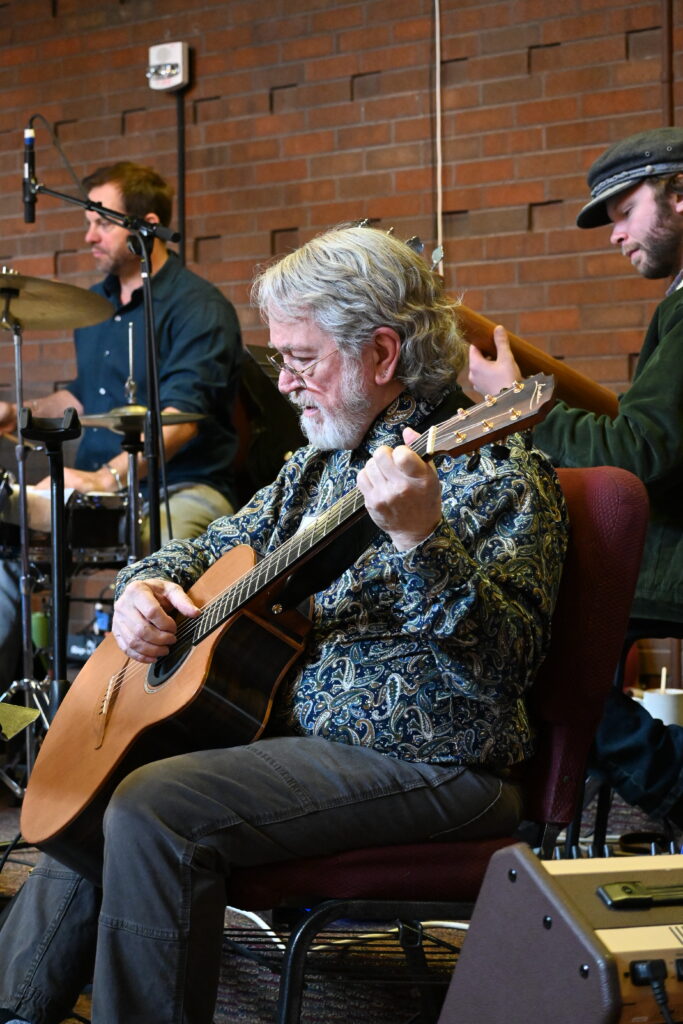 A member of our worship band CommonTime sits in the foreground playing guitar, while two of his bandmates make music alongside him in the background.